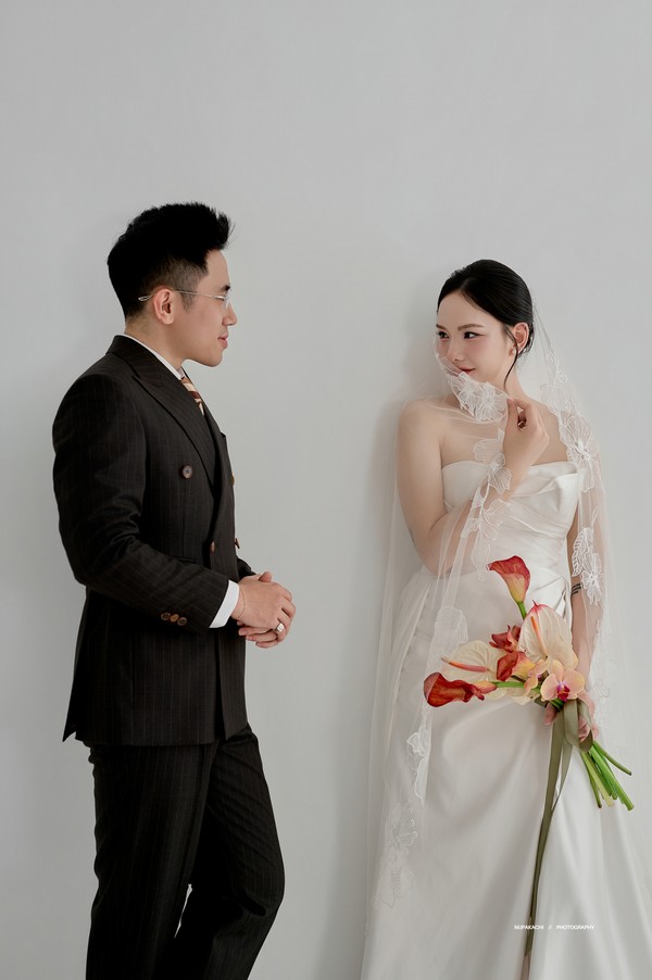 Chú rể Lê Hoàng và cô dâu tạo dáng trang trọng bên phông trắng