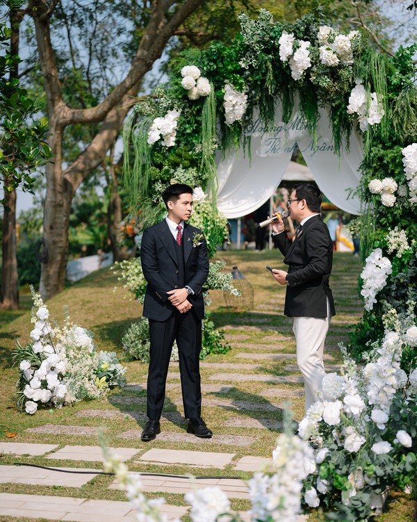 Chú rể chờ đón cô dâu tại lễ đường ngoài trời bên vòm hoa trắng