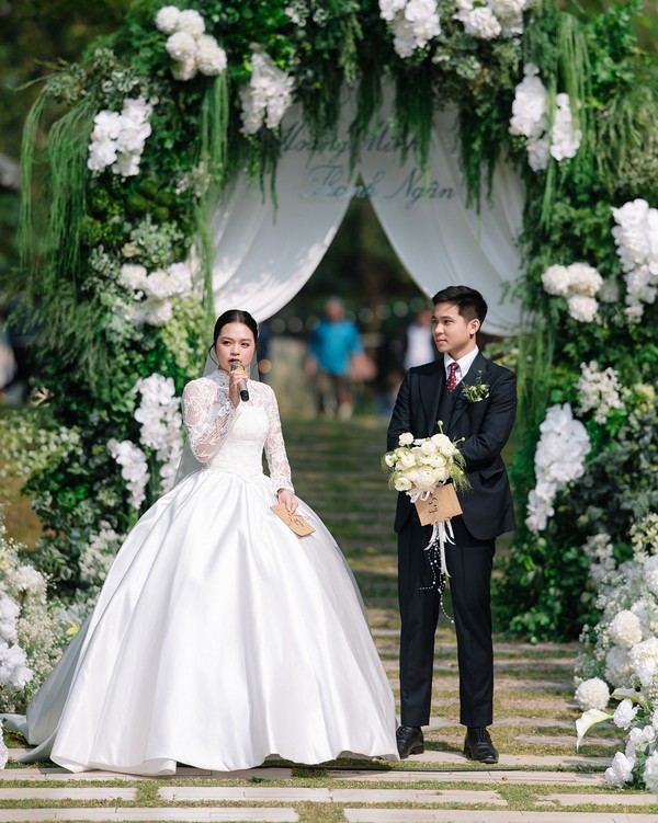 Đôi uyên ương đứng trước vòm hoa cưới lộng lẫy dưới ánh nắng